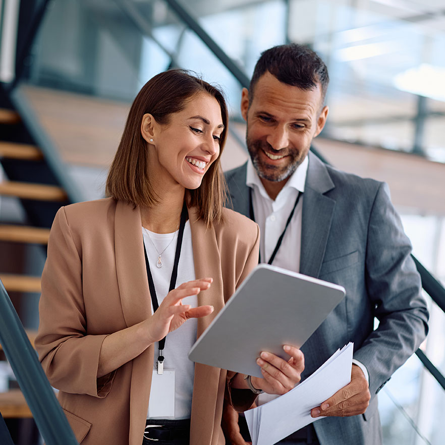 a man and a woman smiling looking at a tablet in their workplace